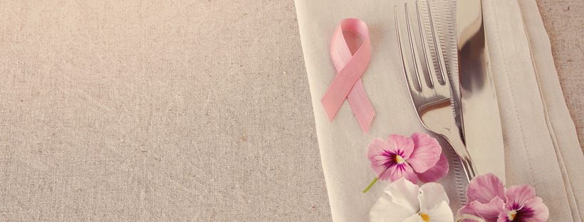 Pink ribbon kept on table napkin along with cutlery